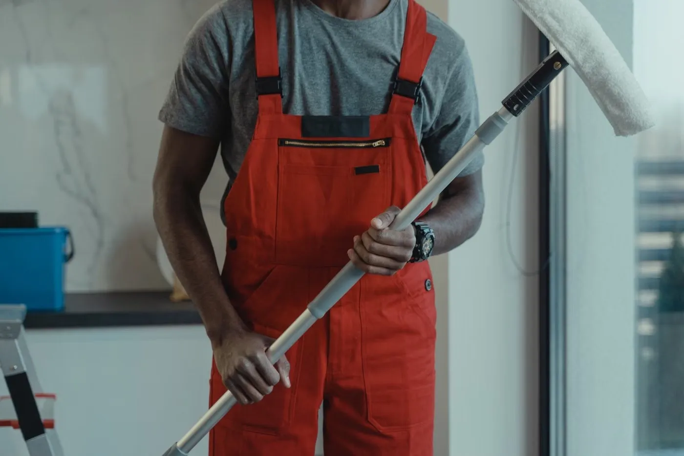 Cleaner in red overalls holding a window cleaning pole