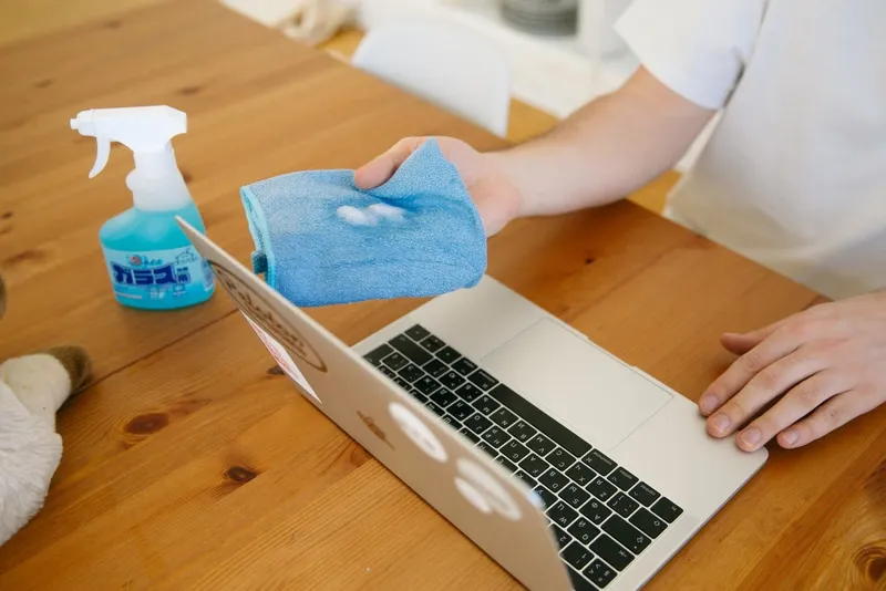Person wiping a laptop with a cloth and cleaning spray