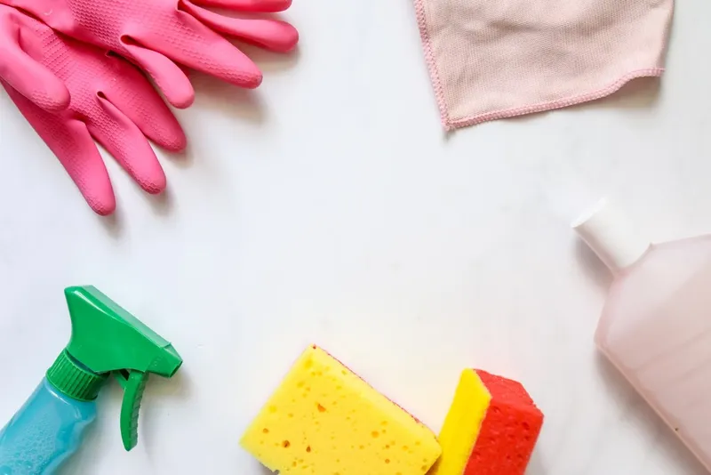 Rubber gloves, sponges and a spray bottle on a white surface