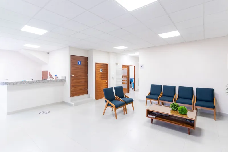 A clean, empty clinic waiting room with blue chairs and a reception counter