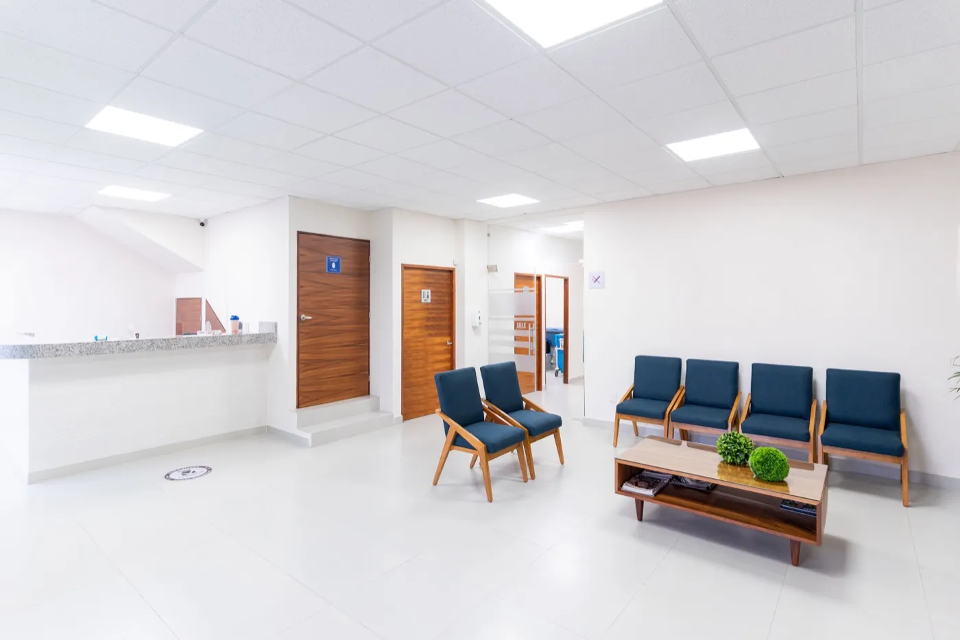 A clean, empty clinic waiting room with blue chairs and a reception counter