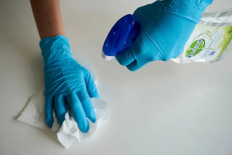 Gloved hand wiping a surface with disinfectant spray