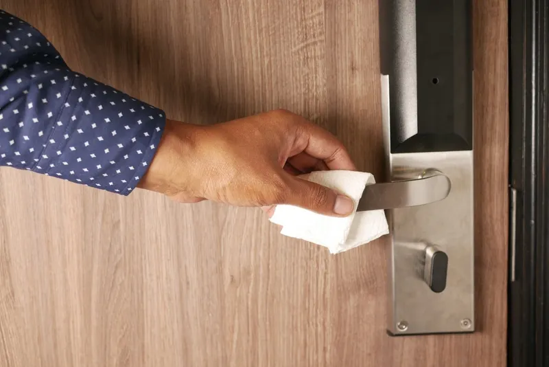 Hand wiping a door handle with a tissue
