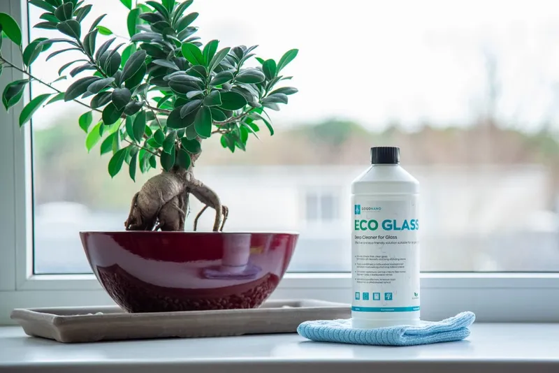 Eco glass cleaner and a microfibre cloth on a windowsill beside a bonsai