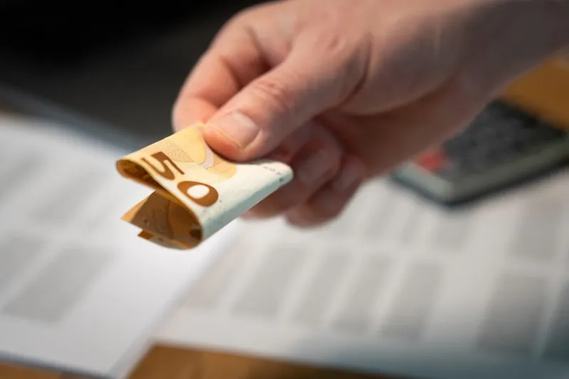 Hand holding a folded euro banknote over paperwork