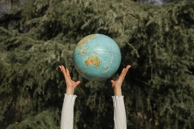 Hands holding up a globe against green trees