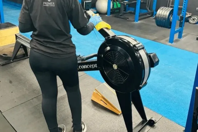 Premier cleaner wiping down a rowing machine in a gym