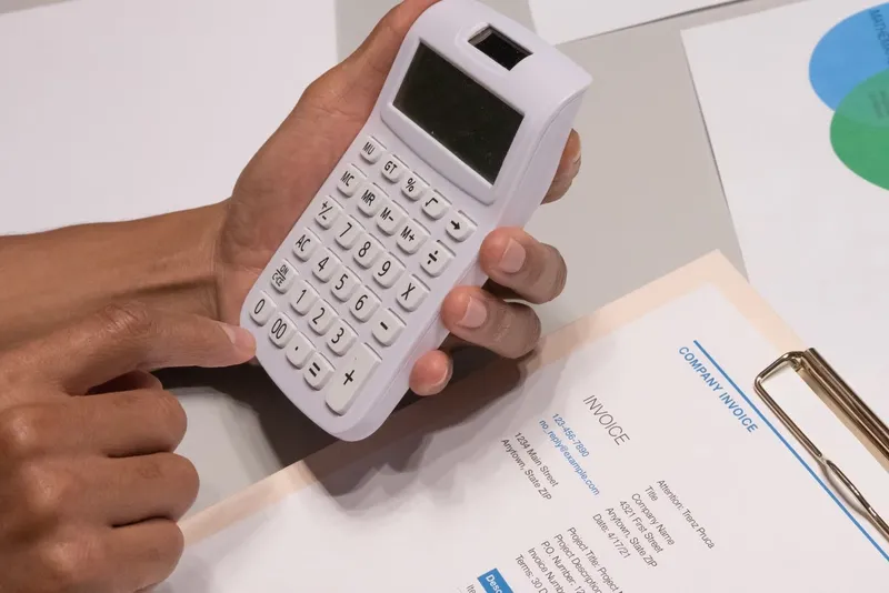 Hands holding a calculator over a company invoice
