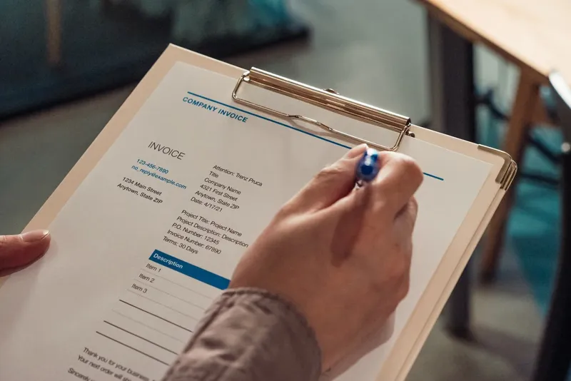Hand holding a company invoice on a clipboard with a pen