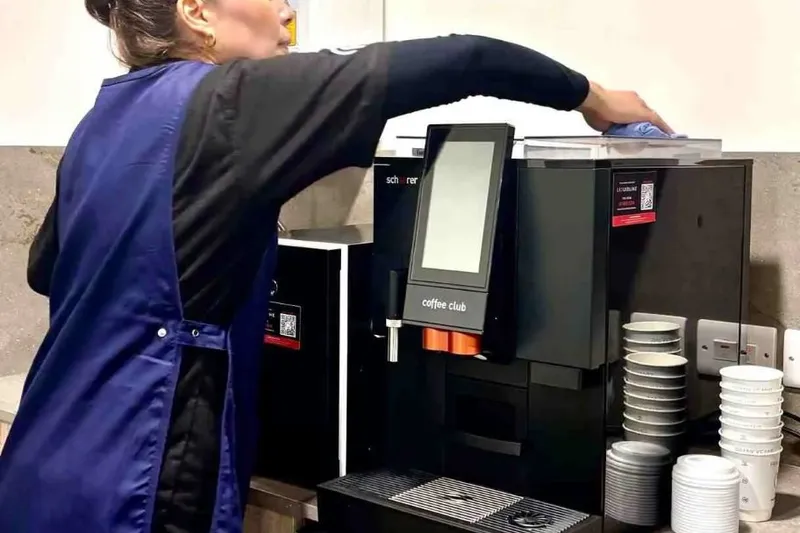 Premier cleaner wiping a coffee machine in an office kitchen