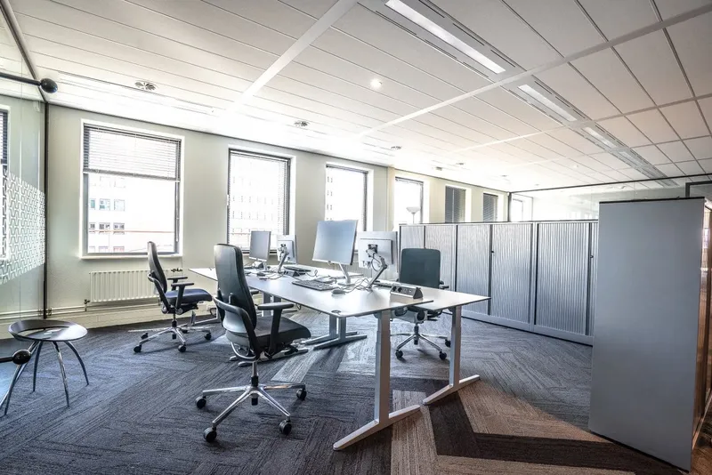 A tidy open-plan office with clear desks and clean carpet tiles