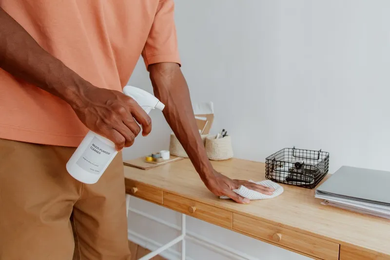 Person spraying and wiping a wooden desk