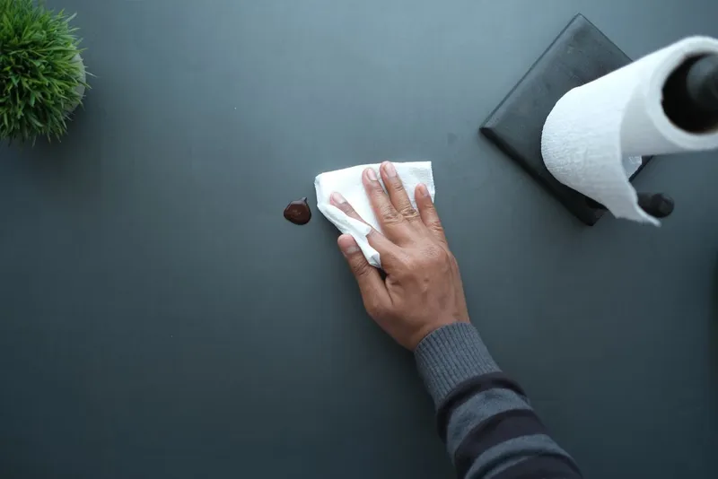 Hand wiping a dark tabletop with a paper towel